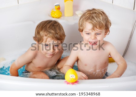 Happy siblings: Two little twins boys having fun with water by taking bath in bathtub