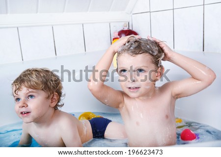 Happy siblings: Two little twins boys playing together with water by taking bath in bathtub