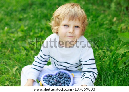 Happy little toddler boy on pick a berry farm picking blueberries in bucket, outdoors