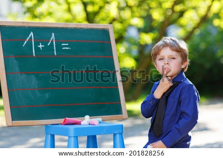 Serious little boy at blackboard practicing mathematics, outdoor school or nursery. Back to school concept