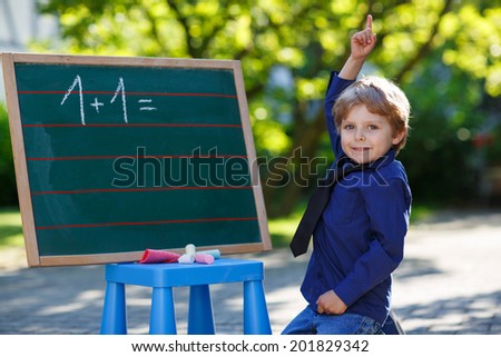 Little boy at blackboard practicing mathematics, outdoors. Back to school concept.
