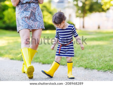 Mother and little adorable daughter in yellow rubber boots, family look, playing with duck toys in summer park