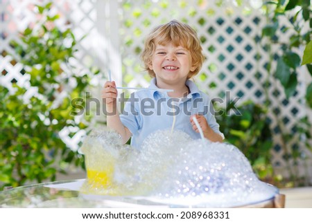 Happy little boy making experiment with colorful soap bubbles and water, outdoors.