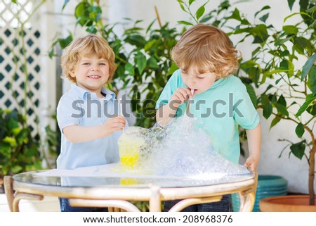 Two happy children making experiment with colorful soap bubbles and water, outdoors.