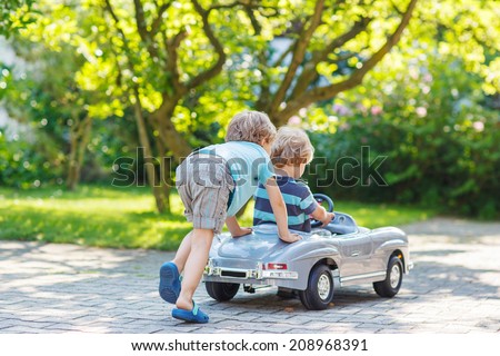 Two happy children playing with big old toy car in summer garden, outdoors.