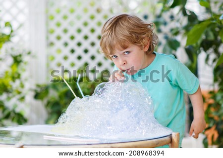 Happy little boy having fun and making experiment with colorful soap bubbles and water, outdoors.
