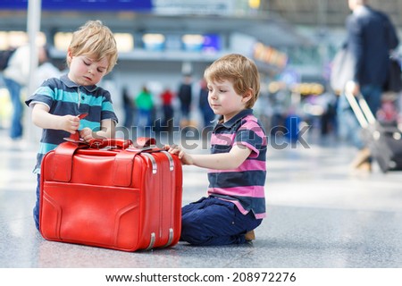 Two little sibling boys having fun and going on vacations trip with suitcase at international airport, indoors.