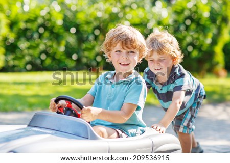 Two happy sibling boys playing with big old toy car in summer garden, outdoors. Selective focus on child in car.