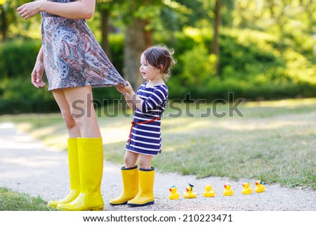 Mum and little adorable girl in yellow rubber boots, family look, in summer park