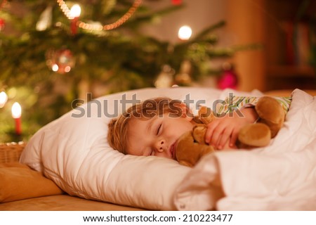 Little cute blond boy sleeping under Christmas tree and dreaming of Santa at home, indoors