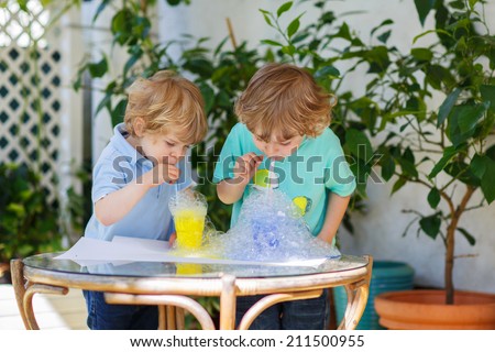 Two happy sibling boys making experiment with colorful soap bubbles and water, outdoors.