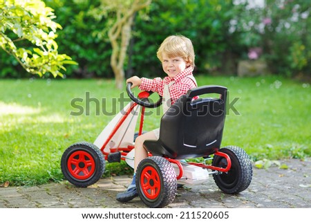 Active little boy of 3 years driving pedal car in summer garden, outdoors.