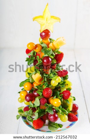 Creative and novel fruit Christmas tree with different berries, fruits and mint, healthy snack on Christmas table or New Year Eve