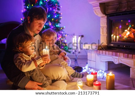 Young father and his two little sons sitting by a fireplace on Christmas time. Selective focus on one child.