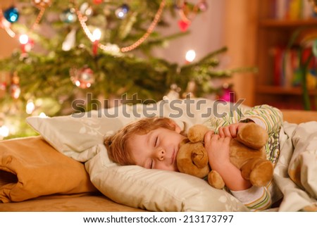 Little adorable blond boy sleeping under Christmas tree and dreaming of Santa at home, indoors
