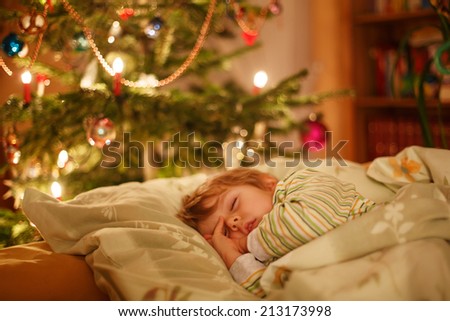 Little cute child sleeping under Christmas tree and dreaming of Santa at home, indoors