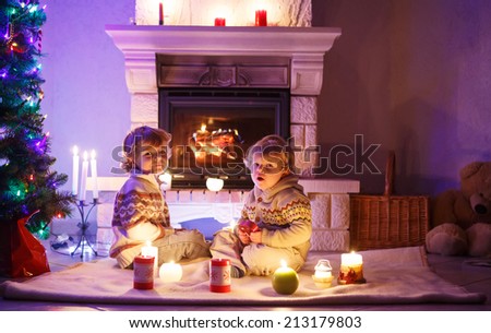 Two little children sitting by a fireplace at home on Christmas time