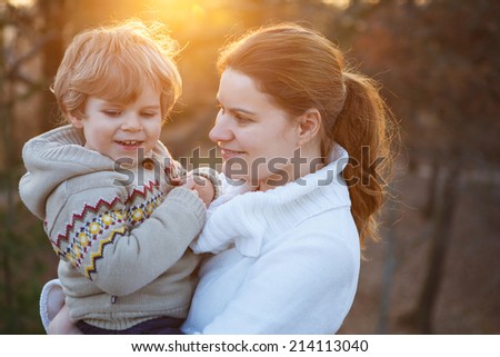 Young caucasian woman and little son hugging in evening light, outdoors