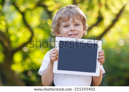 Adorable happy little child holding tablet pc, outdoors. Preschool boy learning with modern technology.