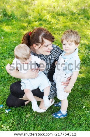 Happy caucasian family of three: Young mother and two little sibling boys in summer park, Europe