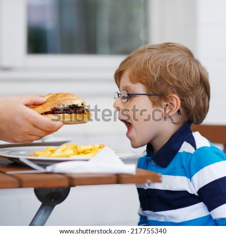 Cute little child eating fast food: french fries and hamburger in cafe. Square format.