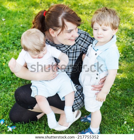Happy caucasian family of three: Young mother and two little sibling boys in summer park, Europe.  Square size.