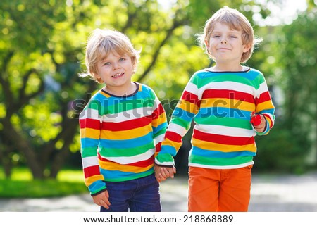 Two little brothers in colorful clothing walking hand in hand and hugging in summer or autumn garden. Brother love