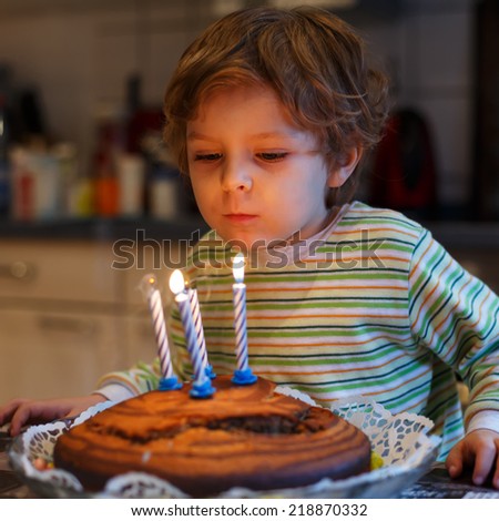Adorable four year old child celebrating his birthday and blowing off the candles on the cake, indoor. Square format.