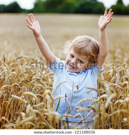 Happy smiling little kid boy with blond hairs having fun in wheat field in summer, outdoors. Square format.