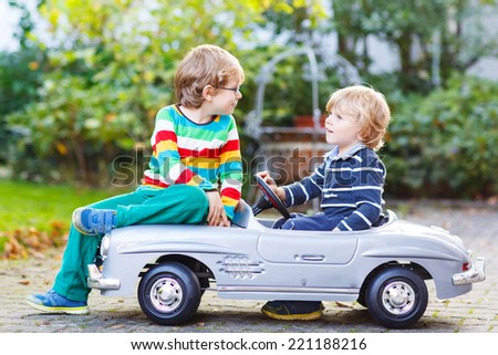 Two happy kids playing with big old toy car in summer garden, outdoors. Siblings and friends on warm day.