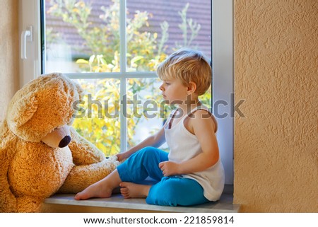 Lovely cute child of two years sitting near window with big toy bear