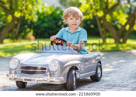 Little preschool boy driving big toy car and having fun, outdoors.