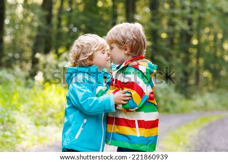 Two little sibling children in colorful waterproof raincoats and rubber boots hugging in autumn forest together. Brother love
