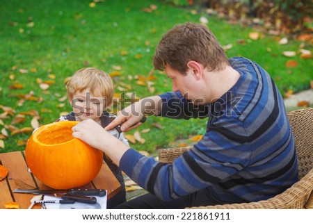 Young man and little toddler boy having fun with making halloween pumpkin face