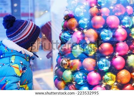 Adorable little boy looking through the display window at Christmas decoration in the shop