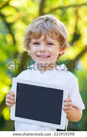 Adorable happy little kid boy holding tablet pc, outdoors. Preschool child learning with modern technology.