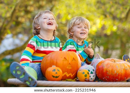 Two little sibling boys making jack-o-lantern for halloween in autumn garden, outdoors. Happy family having fun together