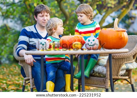 Dad and his two little sons making jack-o-lantern for halloween in autumn garden, outdoors. Happy family of three having fun together