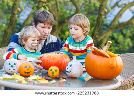 Young father and his two little sons making jack-o-lantern for halloween in autumn garden, outdoors. Happy family of three having fun together