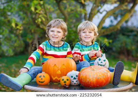 Two little friends boys making jack-o-lantern for halloween in autumn garden, outdoors. Happy family having fun together