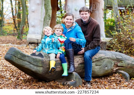 Happy family of four sitting on a bench in autumn park: mother, father and two little sibling kid boys.