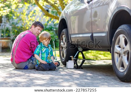 Happy father and his little toddler boy repairing car and changing wheel together on warm sunny day, outdoors. Dad teaching his son.