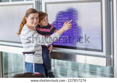 Young mother and little kid boy at the international airport, looking on flight board at terminal, going on vacation.