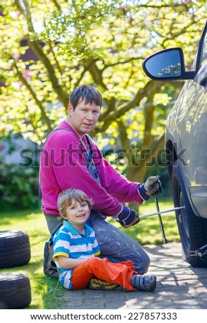 Happy father and his little kid son repairing car and changing wheel together on warm sunny day, outdoors. Dad teaching his son.