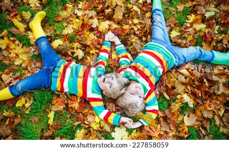 Two little twin boys lying in autumn leaves in colorful clothing. Happy siblings having fun in autumn park on warm day.