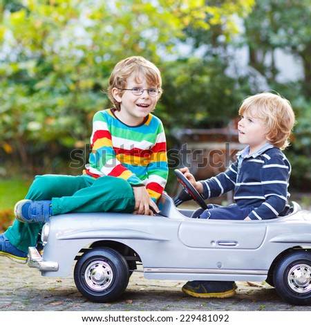 Two happy kids playing with big old toy car in summer garden, outdoors. Siblings and friends on warm day. Square format.