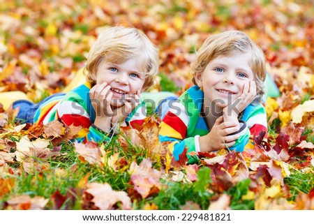 Two happy children lying in autumn leaves in colorful clothing. Happy siblings having fun in autumn park on warm day.