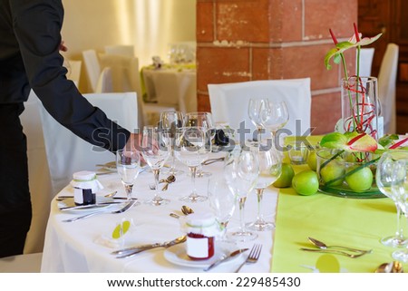 Waiter in black serving elegant table set in white and green with apples for wedding or event party in a castle