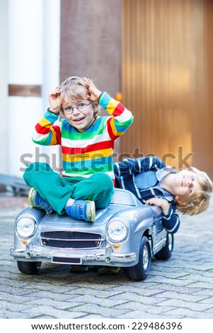 Two happy kids playing with big old toy car in summer garden, outdoors. Siblings and friends on warm day. Selective focus on one boy.