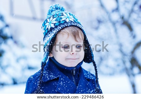 cute little child in winter clothes with falling snow. Kid enjoying and catching snowflakes, outdoors on cold day.